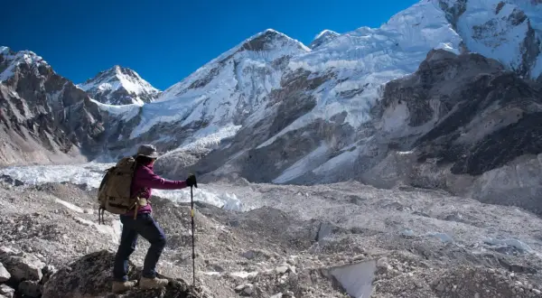 Turystka z plecakiem i kijkami trekkingowymi podziwia majestatyczne szczyty Himalajów w okolicy **Mount Everest Base Camp**.