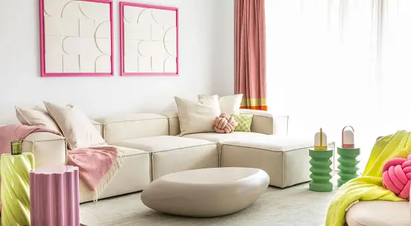 Salon moderne avec canapé crème, coussins roses et verts, tables d'appoint colorées. L'association de couleur peinture crée une ambiance joyeuse.