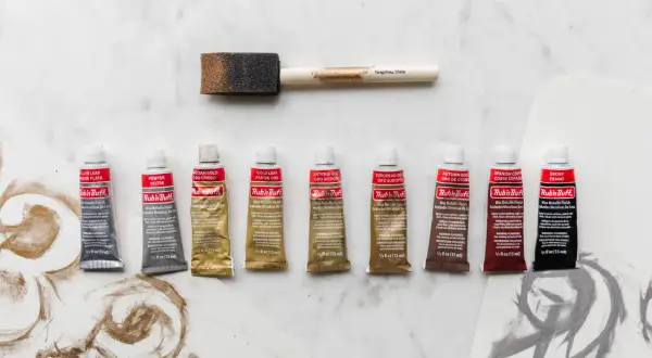 A collection of Rub'n Buff wax metallic finish tubes in various colors, alongside a foam applicator brush, ready to add a beautiful sheen to any project.