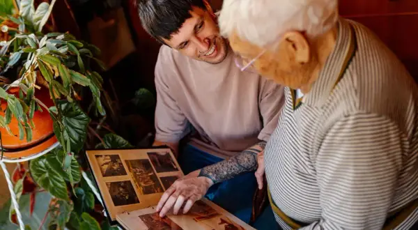 Un jeune homme et une personne âgée regardent un album photo.