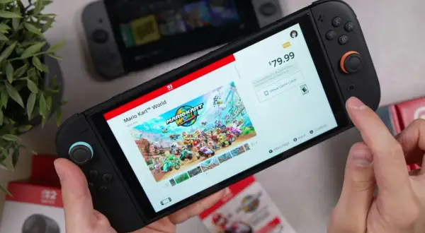 Ręce trzymają konsolę Nintendo Switch, na ekranie której wyświetla się gra Mario Kart World. To świetny przykład gry ruchowej na Nintendo Switch.