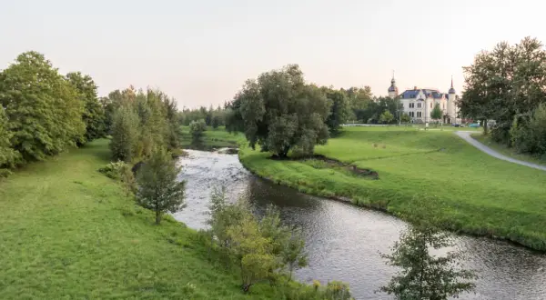 Idyllischer Flusslauf mit grünen Ufern und einem Schloss im Hintergrund. Ein perfekter Ort für Radwege Geheimtipp-Touren.