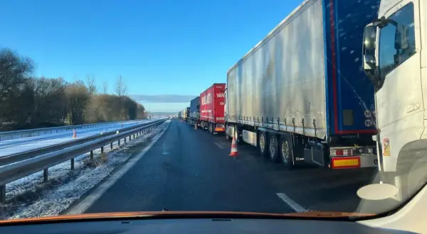 Longue file de véhicules poids lourds à l'arrêt sur une autoroute enneigée sous un ciel bleu clair.