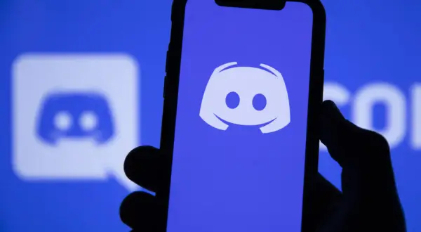 Dłoń trzyma smartfon z logo Discord. Aplikacja ta służy do komunikacji, więc jeśli zastanawiasz się "discord co to", to właśnie ją widzisz.