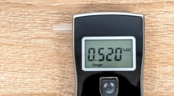 Alkomat z wyświetlaczem pokazującym 0.520 %BAC i napisem "Danger" na drewnianym tle.