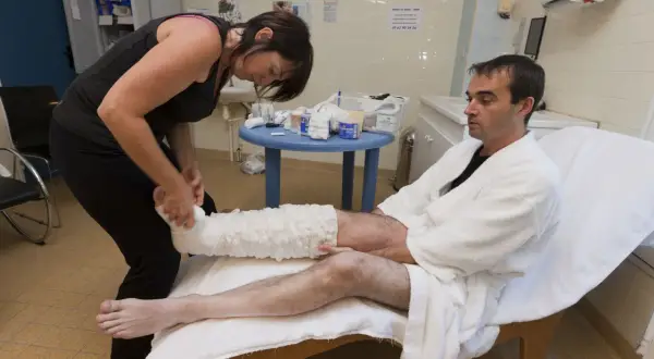 Une thérapeute applique un bandage compressif sur la jambe d'un homme, étape clé dans le traitement du lymphoedème.