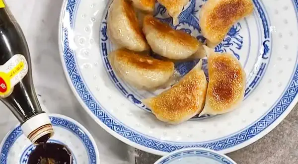 Stekta vegetariska dumplings serveras på en blåvit tallrik. Sojasås hälls upp i en liten skål. Ett perfekt vegetariska dumplings recept!