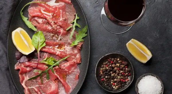 Delicioso carpaccio de ternera con rúcula, limón y pimienta. Acompañado de una copa de vino tinto.