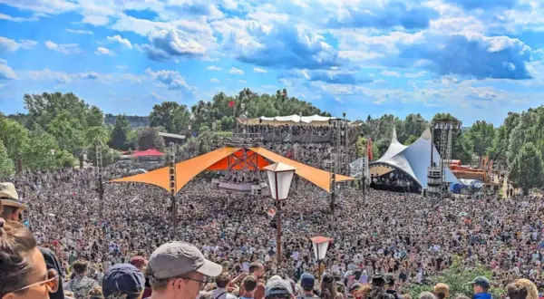 Tausende feiern auf dem Fusion Festival Ort unter blauem Himmel. Bunte Zelte und Bühnen prägen die Szenerie.