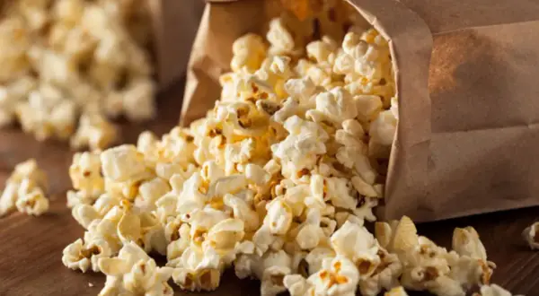 Frischer Popcorn fließt aus einer Papiertüte. Perfekt für kalorienarme Snacks beim Filmabend.