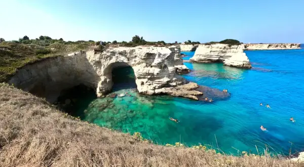 Scogliere bianche e mare cristallino nel Salento, con persone che nuotano e si godono il sole.