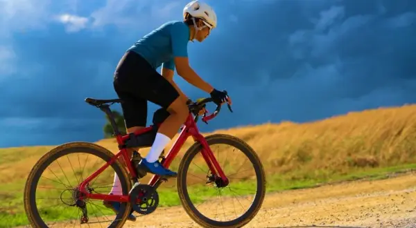 Kobieta w kasku i sportowym stroju pokonuje szutrową trasę na czerwonym rowerze gravel.