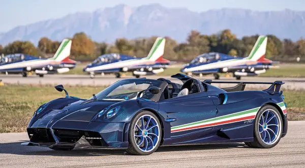 Niebieski Pagani Huayra Roadster z włoską flagą na boku, obok samolotów akrobacyjnych. Jego pagani huayra cena jest astronomiczna.