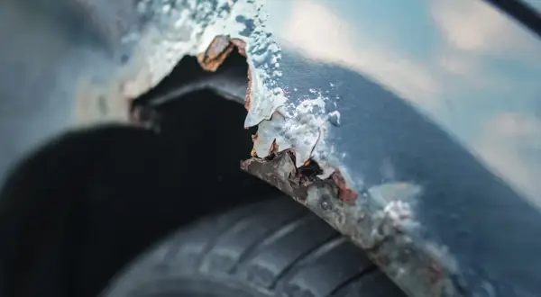 Detaljerad bild av rostig bilskärm. En del av skärmkanten har flagnat och blottar metallen under, redo att laga rost bil. Däcket syns nedtill.