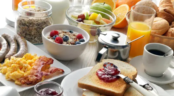 Ein reichhaltiges Frühstück in Görlitz: Rührei, Speck, Würstchen, Müsli, Obst, Toast mit Marmelade, Saft und Kaffee.