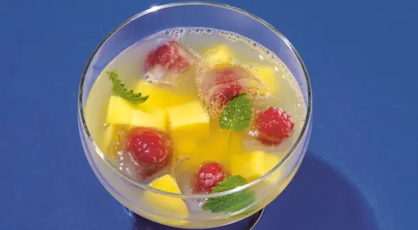 Erfrischende alkoholfreie Bowle mit Mango, Himbeeren und Minze in Eiswürfeln.