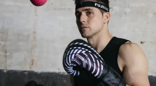 Bokser w rękawicach i opasce FUJIMAE, japoński producent sprzętu sportowego, ćwiczy z piłką refleksyjną.