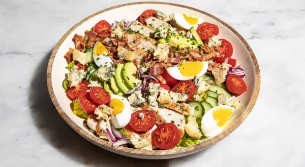 Ein üppiger Cobb Salad deutsch mit Hähnchen, Speck, Ei, Avocado, Tomaten und Blauschimmelkäse.