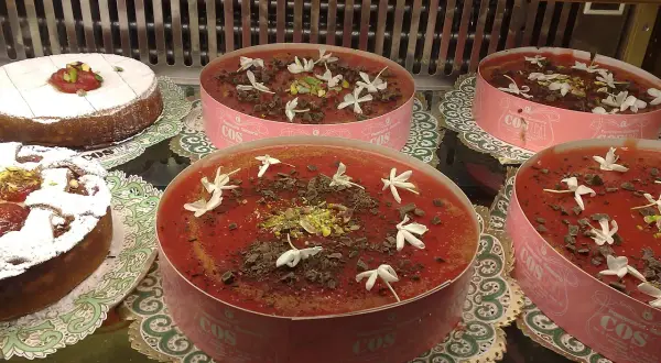 Deliziosi dolci in vetrina, tra cui un tortino con zucchero a velo e un invitante gelo di anguria decorato con fiori bianchi e scaglie di cioccolato.