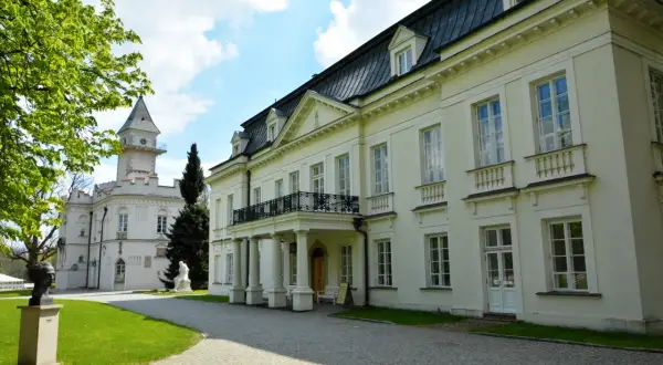 Pałac Radziejowice noclegi cennik: biały pałac z wieżą, zielony trawnik, rzeźby, drzewa, błękitne niebo z chmurami.