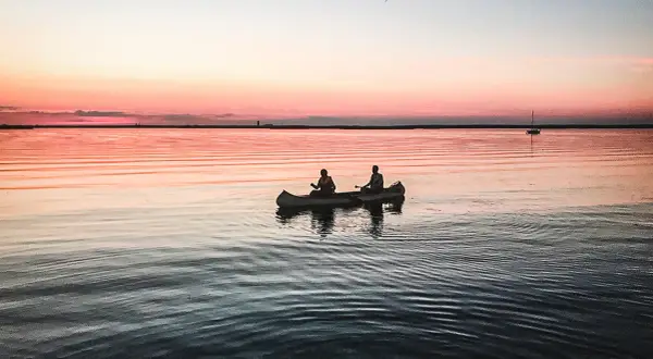 Två personer paddlar kanot i solnedgången. En perfekt plats att fundera på vart ska man resa i juli.