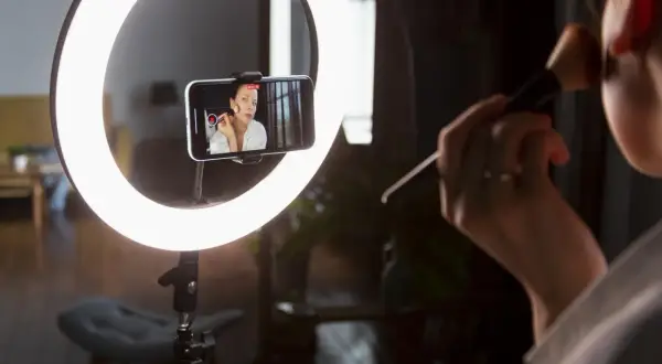 Idealne światło do makijażu: ring light oświetla twarz kobiety nagrywającej tutorial na telefonie.