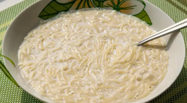 Zupa mleczna z makaronem, podana w misce z motywem kwiatowym, na zielonej podkładce.