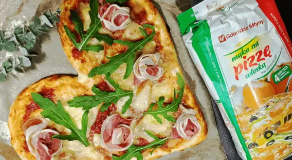 Serce z pizzy z rukolą i szynką, obok mąka do pizzy. Idealne do pieczenia pizzy w piekarniku.