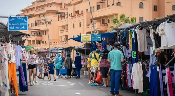 Gente comprando ropa en puestos del paseo marítimo de Garrucha. Edificios naranjas al fondo.
