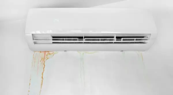 Condizionatore che perde acqua, lasciando macchie umide e colorate sul muro bianco.