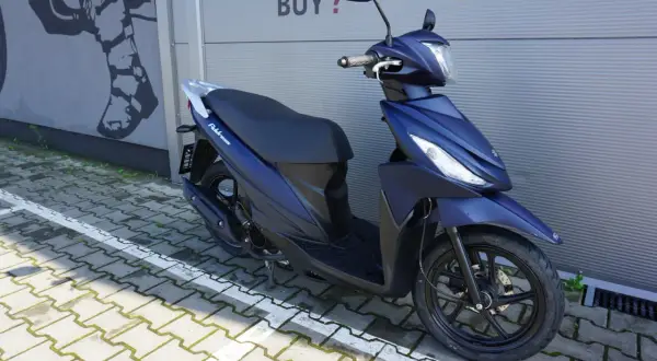Elegancki, granatowy skuter Suzuki Address 110 zaparkowany na kostce brukowej.