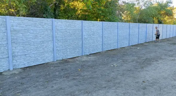 Mężczyzna z łopatą przy betonowym ogrodzeniu, zastanawia się, jak podwyższyć ogrodzenie betonowe, by zyskać więcej prywatności.