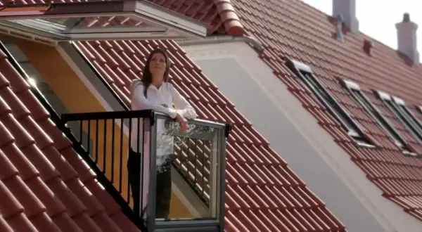 Kobieta na balkonie wychodzącym z okienka w dachu, podziwia widok.