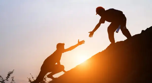Siluetas de dos hombres ayudándose a subir una colina al atardecer. Un gesto de apoyo que contrasta con las frases de invalidación emocional.