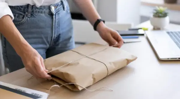 Ręce wiążą sznurkiem paczkę owiniętą w papier. Gdzie nadać mini paczkę Poczta Polska?
