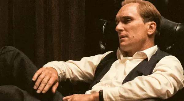 Robert Duvall jako Tom Hagen w fotelu, zamyślony, w białej koszuli i kamizelce.