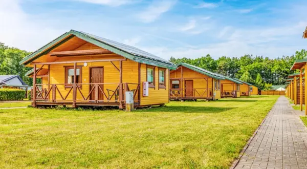 Drewniane domki letniskowe w ośrodku Błękitna Laguna Karwia, z werandami i panelami słonecznymi na dachach, stoją na zielonej trawie.