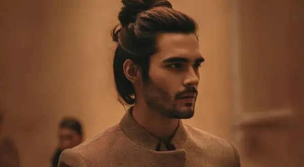 Un homme au chignon bas homme élégant, portant une veste texturée, pose avec assurance.