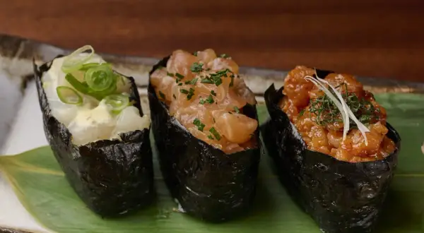Drei Gunkan-Maki-Sushi mit Lachs, Garnelen und Fisch, garniert mit Frühlingszwiebeln und Kräutern.