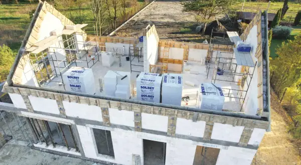 Budowa domu w toku. Widoczna ściana szczytowa z elementami konstrukcyjnymi i materiałami budowlanymi.