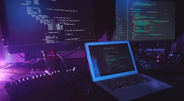 Code informatique sur plusieurs écrans, avec un clavier et un ordinateur portable. Le code Python utilise la méthode `strip` pour nettoyer les chaînes.