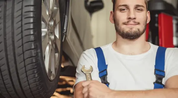 Uśmiechnięty mechanik z kluczem w dłoni, gotowy do pracy przy aucie hybrydowym. To on stoi za nowymi certyfikatami dla mechaników.