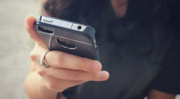 Dłoń z pierścionkiem trzyma telefon. Zastanawiasz się, dlaczego telefon wolno się ładuje? Może to wina kabla lub starej baterii.