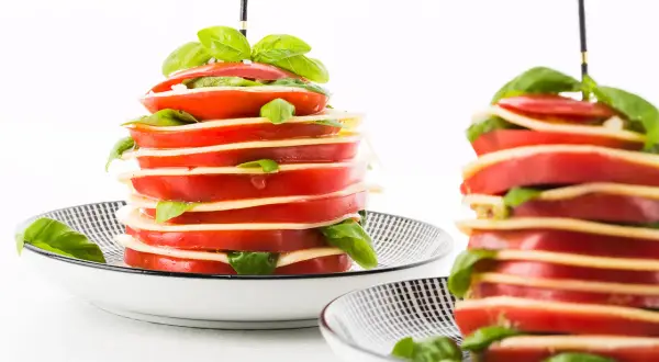 Torres de tomates y mozzarella con albahaca, unos entrantes típicos de Francia, servidos en platos con diseño geométrico.