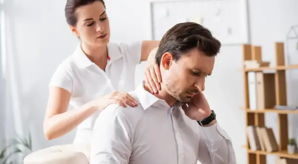 Une thérapeute prodigue un massage au bureau à un homme d'affaires, soulageant ses tensions au cou et aux épaules.
