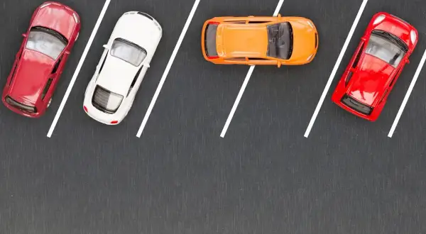 Cztery samochodziki na parkingu, gotowe do równoległego parkowania. Czerwony, biały, pomarańczowy i znów czerwony.