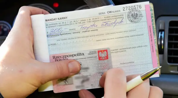Ręka trzyma mandat karny na 300 zł, wystawiony za parkowanie na zakazie. Obok dowód osobisty.