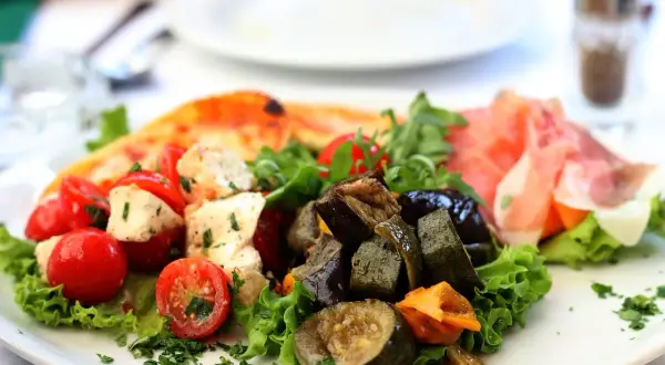 Assiette d'antipasti colorée : tomates cerises, mozzarella, légumes grillés, jambon cru et une part de pizza. Une recette d'antipasti parfaite pour l'été.