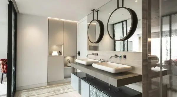 Un moderno baño con dos lavabos sobre encimera de piedra, espejos circulares colgantes y armarios integrados. Se puede hacer un baño en una habitación así.