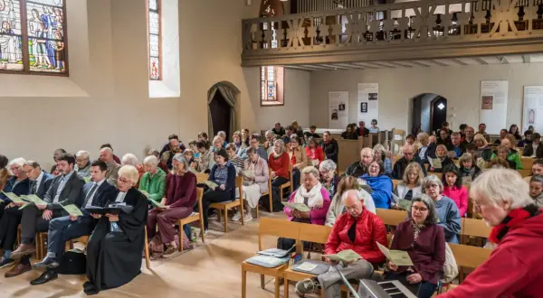 Menschen sitzen in einer Kirche und singen. Dies ist ein Beispiel dafür, was ist eine Freikirche: eine Gemeinschaft, die sich selbst organisiert.